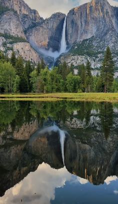 yose falls reflected in the still water of a lake with trees and grass around it