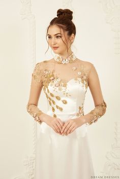 a woman in a white dress with gold embroidered sleeves and an open neckline is posing for the camera