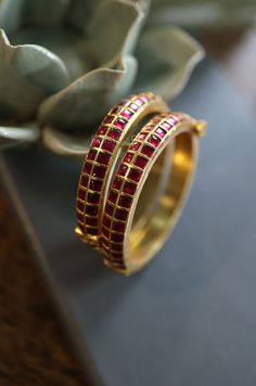 These contemporary Kundan bangles are the perfect accessory for any modern wardrobe. The gold-plated finish adds a touch of opulence and sophistication to the design, creating a luxurious contrast against the vibrant Kundan stones. The radiant red Kundans, with their timeless elegance and fiery brilliance, exude a sense of passion and allure. Let their timeless beauty and timeless appeal adorn your wrists, adding a touch of glamour and sophistication to every occasion. Closure - Screw Weight- 99gm Handcrafted in Jammu and Kashmir Paisley Pop travels the depths of India to learn techniques and crafts from deep down in the local markets and villages. We give utmost importance to our quality and packaging. Our goal is to ensure you receive exactly what you are looking for and for your experie Red Temple Jewelry Bracelets For Formal Occasions, Red Stone Bangles, Kundan Bangles Design, Kemp Bangles, Designer Bangles, Red Bangles, Indian Accessories, Kundan Bangles, Gold Bangle Set