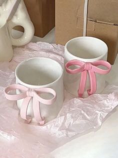 two white mugs with pink bows on them sitting on a table next to boxes