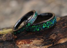 two wedding rings with green and blue opal inlays sitting on a piece of wood