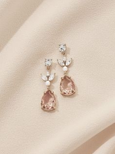 two pairs of earrings on top of a white cloth with pearls and crystal stones in the middle