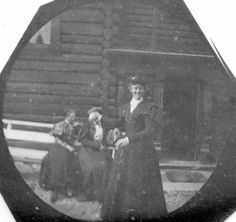 an old black and white photo of three women in front of a log cabin,