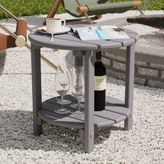 a small table with two wine glasses and a book on it in the middle of a gravel area