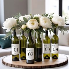 four wine bottles with flowers in them sitting on a wooden table next to a couch