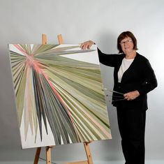 a woman standing next to an easel holding up a large piece of art that is on display