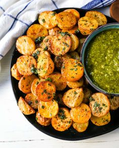 a black plate topped with fried potatoes next to a bowl of pesto dipping sauce