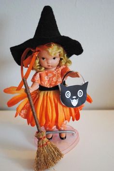 a doll dressed as a witch with a black cat on her broom and orange dress