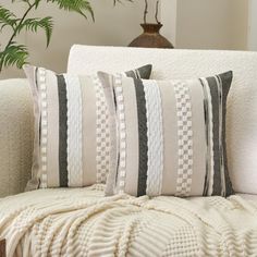 a white couch with black and white striped pillows on it's back, next to a potted plant