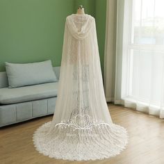 a white wedding dress on display in front of a couch and window with green walls