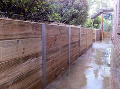 a long wooden fence next to a brick building with trees growing on top of it