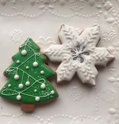 two decorated cookies sitting on top of a white plate next to a green christmas tree