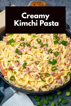 creamy kimchi pasta with green onions and ham in a skillet on a table