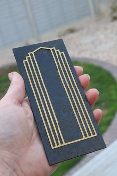 a hand holding a black and gold business card in front of a circular area with grass