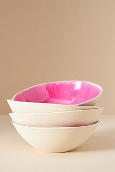 three white and pink bowls stacked on top of each other in front of a beige background