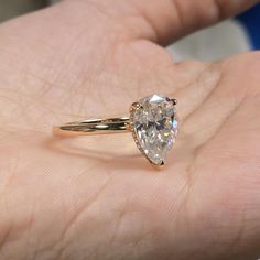 a close up of a person's hand holding a ring with a pear shaped diamond