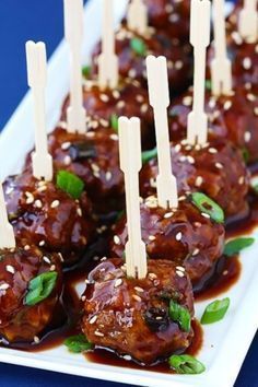 several skewered meatballs with sauce and garnish on a white plate