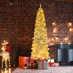 a white christmas tree with gold lights in front of a brick wall and presents on the floor