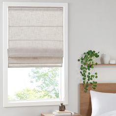 a bedroom with a bed, nightstand and window covered in roman shades on the windowsill