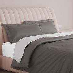 a bed with grey and white comforters in a bedroom next to a pink headboard