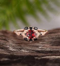 a red and black diamond ring sitting on top of a piece of tree bark with leaves in the background