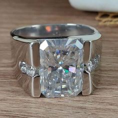 a ring with a large diamond surrounded by smaller diamonds on a wooden table next to a vase