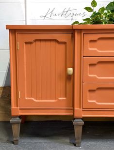 an orange cabinet with three drawers and two plants on the top one drawer is open