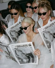 a group of women sitting next to each other in front of a man reading a newspaper