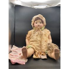 an antique doll sitting on the ground next to other dolls and cloths in a display case