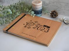 a wooden notebook with a graduation date on the cover next to some candles and greenery