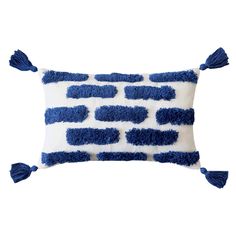 a blue and white pillow with tassels on the edges, in front of a white background