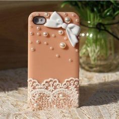 an iphone case with pearls and a white bow on it sitting on a lace tablecloth