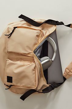 an open laptop and headphones in a backpack on the floor next to a white wall