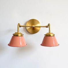 two pink lamps mounted on the wall next to each other with one light turned on