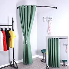 a room with green curtains and clothes hanging on the rack next to a mirror in front of it