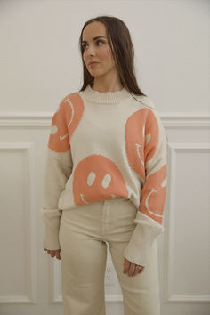 cream knit sweater with orange smiley faces Playful Crew Neck Fall Sweater, Playful Crew Neck Sweater For Fall, Playful Long Sleeve Sweater With Relaxed Fit, Oversized Fun Fall Sweater, Oversized Fun Sweater For Fall, Trendy Smiley Face Tops For Loungewear, Trendy Smiley Face Loungewear Tops, Oversized Playful Sweater For Fall, Playful Oversized Sweater For Fall