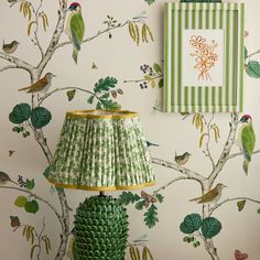 a green lamp sitting on top of a table next to a wallpaper covered in birds