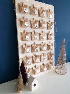 a wooden calendar on a table with christmas trees and lights around it, in front of a blue wall