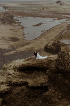 a bride and groom standing on top of a rock in the middle of an open field