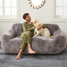 a man sitting on top of a gray couch next to a white dog in his lap