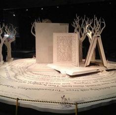 an open book sitting on top of a table covered in paper and tree branches with lights