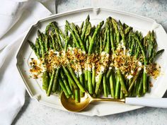 asparagus with sour cream and seasoning on a white platter next to a gold spoon