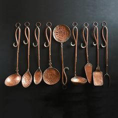 an assortment of copper colored utensils hanging from hooks on a black wall,