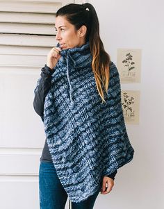 a woman standing in front of a white wall wearing a blue knitted ponchy