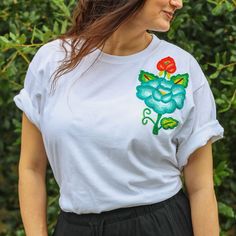 White T-shirt with Hand-Embroidered Flowers Made in Oaxaca, Mexico This white t-shirt is transformed into a piece of art with the famous Oaxacan flower hand-embroidered on the left chest. Each flower is different in color and shape, making each shirt unique. The bright embroidery stands out against the white background, making it a focal point of any outfit. These "flores istmeñas" are designed and transferred onto the fabric, then stretched on a frame for the intricate chain stitch embroidery. Each flower can take up to a week to complete, reflecting the artisan's dedication. Perfect for an effortless, sophisticated look, this t-shirt pairs well with jeans, skirts, or trousers. It's a stunning blend of modern fashion and traditional craftsmanship. Made in Juchitan de Zaragoza, Oaxaca Hand White Crew Neck T-shirt With Floral Applique, White Embroidered Relaxed Fit T-shirt, White Short Sleeve T-shirt With Floral Applique, White Floral Applique Crew Neck T-shirt, Traditional Embroidered Summer T-shirt, Traditional Embroidered Cotton T-shirt, Traditional Embroidered Short Sleeve T-shirt, White Embroidered T-shirt For Summer, Traditional Cotton T-shirt With Multicolor Embroidery