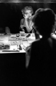 marilyn monroe sitting at a table in front of a mirror with her hands on her face