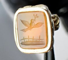 A beautiful antique Georgian gold filled carved carnelian intaglio dove and olive branch seal pendant, dating to circa 1820. Two hundred years ago, this fabulous and finely made George III gold filled intaglio pendant would have been used to seal reconciliatory letters, the pendant has a rectangular bevel-edged carnelian stone which glows the most lovely deep sunset orange when it touches the light, the carnelian finely carved with a dove of peace holding an olive branch in its beak as it flies over a grassy pasture with a wood fence, the carnelian is bezel set in a lovely gold filled setting covered in wonderful scrolling floral and fleur-de-lys decorations with etched and hammered work throughout, the pendant with a built in floral bail-just lovely! The pendant is unmarked. The pendant m Dove And Olive Branch, Deep Sunset, Dove Of Peace, Dove Bird, Sunset Orange, Carnelian Stone, Set Cover, George Iii, Wood Fence