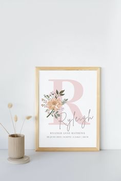 a framed print with the letter r in pink and white, next to a potted plant