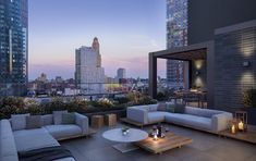 a living room with couches and tables on top of a roof in front of tall buildings