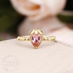 a pink diamond ring sitting on top of a white box with flowers in the background